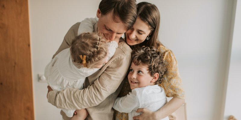 A photo of a family where the parents are hugging their children.