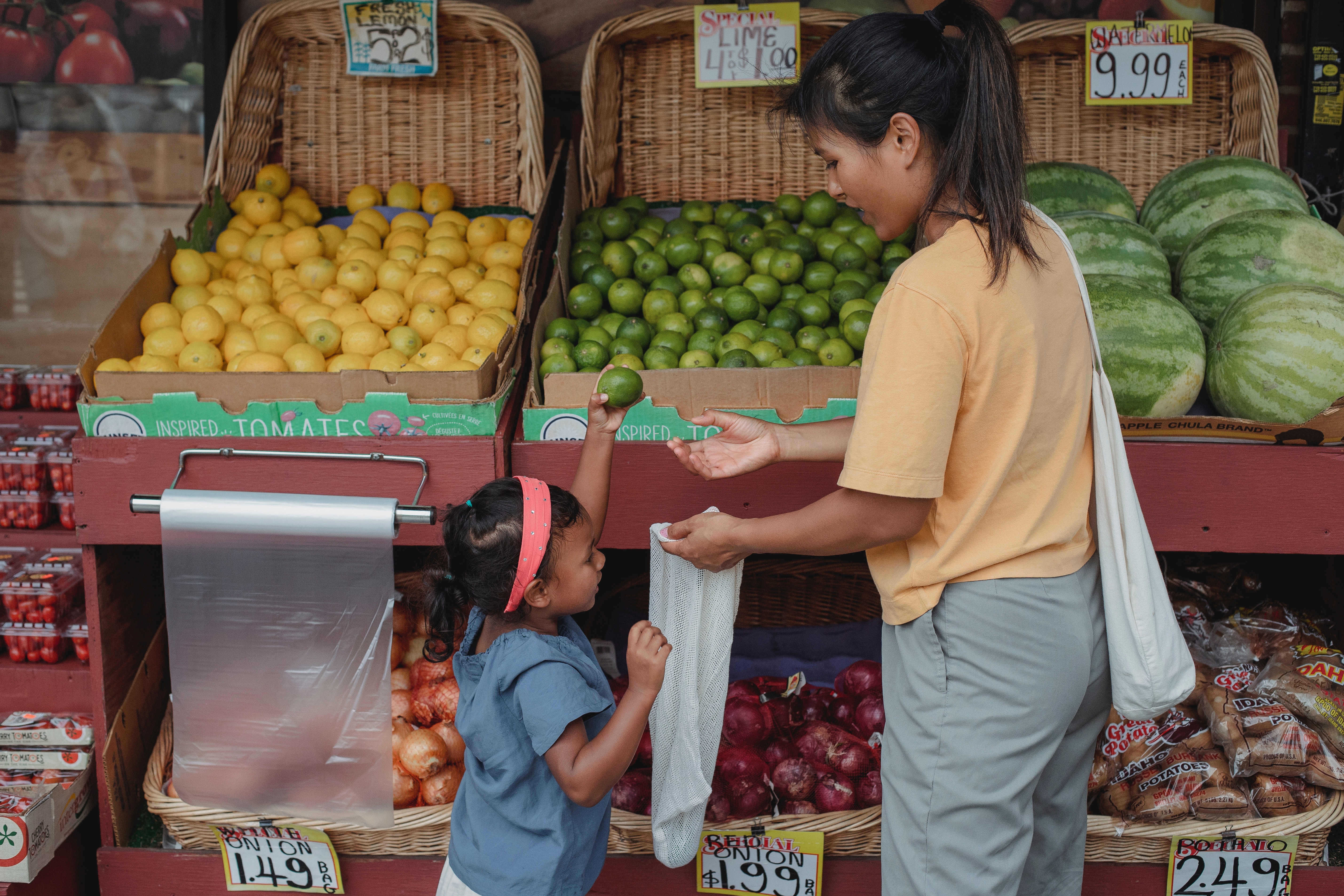 A woman and a small girl in the produce section of a grocery store putting a lime in a produce bag.